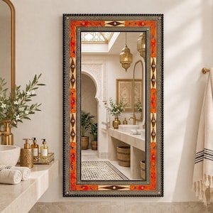 Può includere: Uno specchio da parete rettangolare con una cornice decorativa caratterizzata da un bordo esterno scuro a perline e una vivace bordura interna con motivi floreali arancioni e rossi. La cornice presenta accenti geometrici e intarsi.