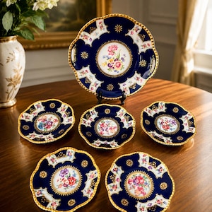 Può includere: Un set di porcellana fine con un design blu navy e oro. I piatti presentano un centro floreale e un bordo smerlato. Il set include un piatto da portata grande e diversi piatti più piccoli, perfetto per una cena formale.