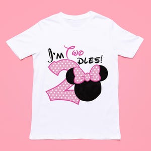 May include: White t-shirt with a pink polka dot number "2" and a pink bow on a black Mickey Mouse head. The text "I'm Two DLES!" is printed on the shirt.
