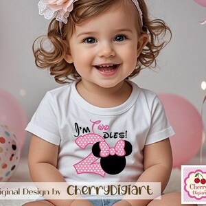 May include: A young girl wearing a white shirt with pink polka dots and the text "I'm Two Dles!" with a pink and black Minnie Mouse graphic. The girl is wearing a headband with a pink flower.
