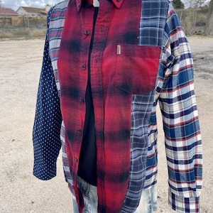 May include: A long-sleeve button-up shirt featuring a patchwork design of various fabrics. The front panel is red and black plaid, the left sleeve is dark blue with white dots, and the right sleeve and side panels feature blue and white plaid.