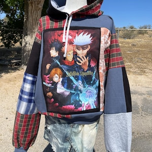 May include: A patchwork hoodie with a graphic of anime characters and the text "Jujutsu Kaisen." The hoodie features a mix of blue, gray, black, and plaid fabric. It has a drawstring hood and long sleeves.