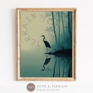 May include: A framed digital art print featuring a dark silhouette of a heron standing by a calm body of water. The background displays a misty forest in shades of teal and beige. The text TERRAIN is visible in the upper left corner of the print.