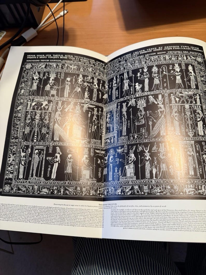 Puede incluir: Una p&aacute;gina de libro que muestra una ilustraci&oacute;n en blanco y negro de la Tabula Isiaca, una antigua tableta de bronce cubierta con intrincadas figuras, jerogl&iacute;ficos y deidades de estilo egipcio, con encabezados en lat&iacute;n y texto en ingl&eacute;s.