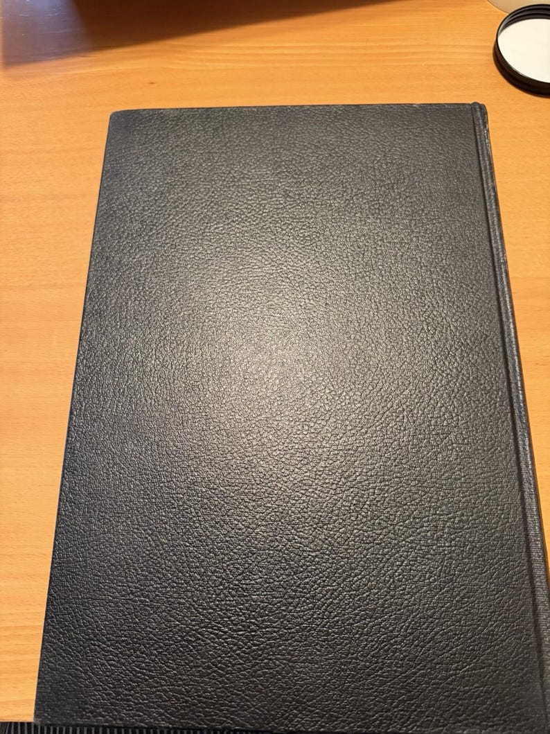 Puede incluir: Un libro de tapa dura rectangular con una cubierta de color azul marino oscuro que presenta una textura distintiva similar al cuero granulado. El libro est&aacute; colocado verticalmente, mostrando una superficie frontal limpia y s&oacute;lida con el lomo visible a la derecha.