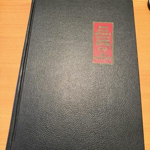 Puede incluir: Un libro de tapa dura negro con un acabado texturizado similar al cuero. En la portada, hay una etiqueta rectangular roja con texto dorado que dice: "Reports, Statistics & Journals of the Legislature of the State of Maine, Vol. II, June 1851".