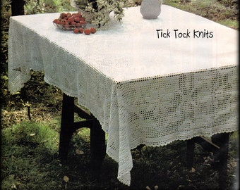 May include: A white crocheted tablecloth with a delicate lace border, set on a wooden table in a garden setting. The tablecloth is decorated with a pitcher and a bowl of red berries. The text "Tick Tock Knits" is visible in the image.