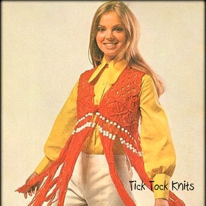 May include: A red crocheted vest with white beads and fringe. The vest is worn over a white button-down shirt and white pants. The model has long blonde hair and is smiling. The text "Tick Tock Knits" is visible in the bottom right corner of the image.