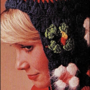 Puede incluir: Una mujer lleva un gorro de punto negro, rojo y rosa con adornos florales. El gorro tiene una solapa larga que cubre las orejas y el cuello. El gorro está hecho con un hilo grueso y tiene una textura peluda. La mujer lleva un suéter rojo y tiene el pelo rubio. El texto "Tick Tock Knits" es visible en la parte inferior de la imagen.