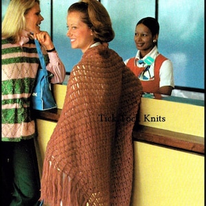 May include: A woman wearing a brown crocheted shawl with fringe. The shawl is draped over her shoulders and has a lacy pattern. The woman is standing in front of a counter with a yellow surface. The text "Tick Tock Knits" is visible on the counter.