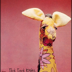 Puede incluir: Un peluche de jirafa amarillo con un patrón floral. La jirafa tiene orejas grandes y está sentada sobre una superficie marrón. El texto "Tick Tock Knits" es visible en la imagen.