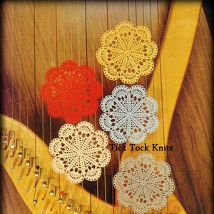 Puede incluir: Cinco doilies de ganchillo en varios colores, incluyendo amarillo, rojo, blanco y azul, están colgados de las cuerdas de un arpa. Los doilies son de diferentes tamaños y tienen un diseño delicado y de encaje. El texto "Tick Tock Knits" es visible en la imagen.