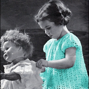 May include: A young girl wearing a light blue crocheted dress with a doll sitting beside her. The girl is holding the doll's arm. The image is in black and white except for the dress, which is in a light blue color.