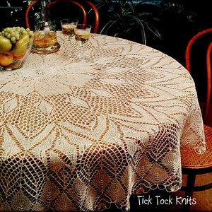 May include: A white crocheted tablecloth with a delicate floral pattern, laid on a wooden table with two chairs. The tablecloth has a scalloped edge and a central motif. The text "Tick Tock Knits" is visible in the bottom right corner.