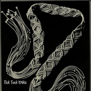 Op de afbeelding: Een witte macramé-ketting met een geometrisch patroon en lange kwastjes. De ketting ligt op een zwarte achtergrond. Tick Tock Knits.