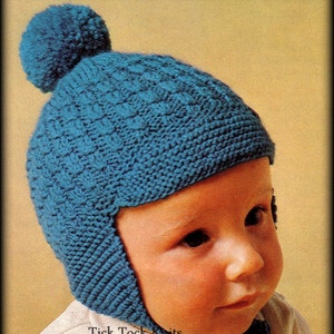 May include: A blue knitted baby hat with ear flaps and a pom pom on top. The hat is made with a textured stitch pattern. The hat is worn by a baby with a white shirt. The text "Tick Tock Knits" is visible in the image.