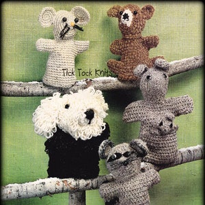 Puede incluir: Cinco marionetas de dedos de crochet, incluyendo un ratón, un oso, un cerdo, un perro y un mapache, se muestran en una rama de madera. Las marionetas son de diferentes colores y tienen varios rasgos faciales. El texto "Tick Tock Knits" es visible en la rama.