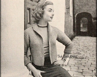 May include: A woman wearing a knitted cardigan with a collared neckline. The cardigan is a light brown color and has a ribbed texture. The woman is standing in front of a brick wall and has her hands on her hips. The text "Tick Tock Knits" is visible in the bottom right corner of the image.