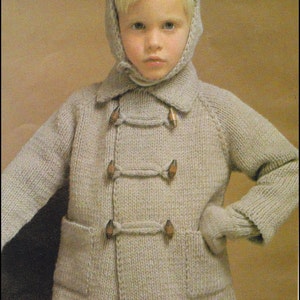 Peut inclure: Un enfant portant un pull à capuche en tricot avec une fermeture à boutons et des mitaines assorties. Le pull est de couleur beige clair et présente un motif en tricot texturé. L'enfant porte un bonnet en tricot beige avec un rabat qui couvre les oreilles. L'image porte le texte "TICK TOCK KNITS" en bas.