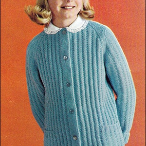 May include: A light blue knitted cardigan with a white collar and buttons. The cardigan has a ribbed texture and a pocket on the front. The model is wearing a grey skirt.