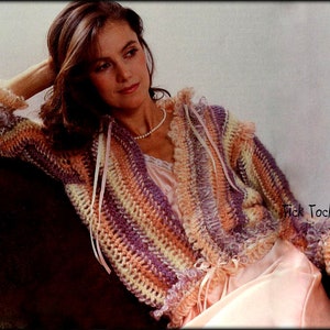 Könnte beinhalten: Eine Frau trägt eine mehrfarbige gehäkelte Strickjacke mit Rüschenbesatz. Die Strickjacke ist gestreift in Rosatönen, Lila und Creme. Die Frau sitzt auf einem braunen Stuhl und hat ihre Hand auf der Armlehne. Der Text "Tick Tock Knits" ist in der rechten unteren Ecke des Bildes sichtbar.