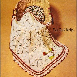 Puede incluir: Una manta de bebé de ganchillo blanco con un borde rojo y un borde festoneado. La manta está en una cesta de mimbre con una almohada floral. El texto "Tick Tock Knits" es visible en la esquina superior derecha de la imagen.