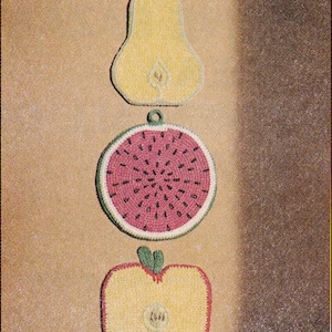 Puede incluir: Tres posavasos de ganchillo con forma de pera, sandía y manzana. La pera es amarilla con hojas verdes, la sandía es roja con semillas negras y la manzana es amarilla con un tallo y hojas verdes. Los posavasos están dispuestos verticalmente sobre un fondo marrón. El texto "TICK TOCK KNITS" está en la parte inferior de la imagen.