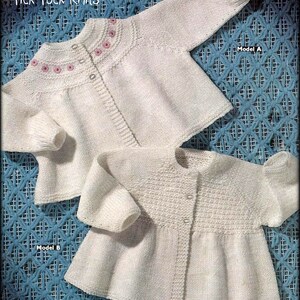 May include: Two white knitted baby sweaters, one with a pink floral design around the neckline, labeled "Model A" and the other with a textured pattern, labeled "Model B".