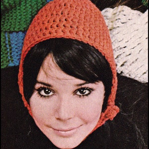 Könnte beinhalten: Nahaufnahme einer Frau, die eine gehäkelte orangefarbene Kapuze trägt. Die Mütze ist mit einem einfachen Stichmuster gearbeitet und hat eine lange, fließende Kapuze.