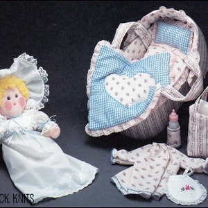 May include: A handmade doll with blonde hair and a white dress, a blue and white gingham baby crib with a pink and white floral blanket, a pink and white striped diaper bag, and a pink and white floral baby bottle.