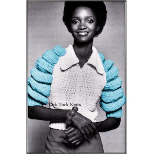 May include: A white crochet top with a collared neckline and blue crochet sleeves. The sleeves are puffed and have a textured design. The model is wearing the top with a black skirt and is holding a beaded necklace.