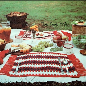 Può includere: Una scena di picnic con una tovaglia bianca, cibo e bevande. Un sottopentola all'uncinetto rosso, bianco e bordeaux con frange contiene posate. Il testo "Tick Tock Knits" è visibile. Sono presenti anche mele, formaggio e insalata.