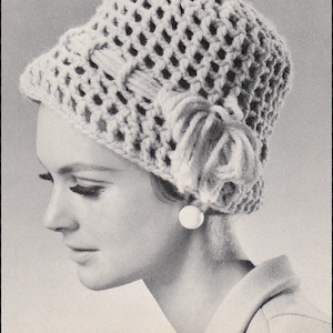 May include: A close-up of a woman wearing a white crocheted hat with a large, crocheted flower embellishment. The hat is a simple, open-weave design. The woman is wearing a white shirt and has her hair pulled back.