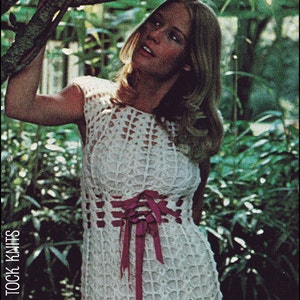 May include: A white crochet dress with a pink ribbon tie at the waist. The dress has a lacy pattern and is worn by a woman with long blonde hair. The background is a lush green garden.