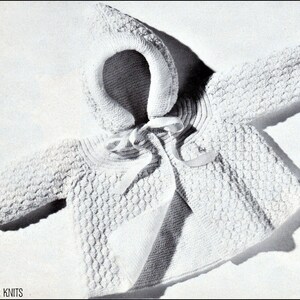 May include: White knitted baby jacket with a hood and a tie closure. The jacket has a textured stitch pattern.