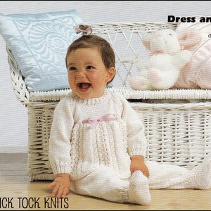 Puede incluir: Un conjunto de vestido y pantalones de punto blanco para bebé con un lazo rosa. El bebé está sentado en un banco de mimbre blanco con un animal de peluche blanco.