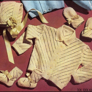 May include: A vintage-style, cream-colored knitted baby set. The set includes a jacket, bonnet, and booties, all adorned with delicate bows. The jacket has a collared neckline and button closures. The booties and bonnet have matching ribbon accents. The set is displayed on a maroon surface.