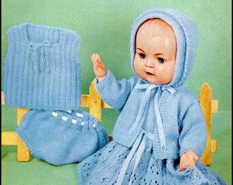 May include: A blue knitted baby doll outfit with a matching hat. The outfit includes a dress, a cardigan, a vest, and a pair of bloomers. The doll is sitting on a wooden fence. The pattern is called "Baby Nylon" and is from "Tick Tock Knits".