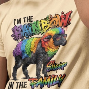 May include: Beige t-shirt featuring a colorful graphic of a sheep with rainbow-colored wool, wearing sunglasses and a black leather jacket. Text on the shirt reads "I'm the Rainbow Sheep in the Family."