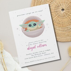 May include: A baby shower invitation featuring a cartoon image of a green alien character in a pod. The text reads "precious cargo on its way!" and invites guests to a shower honoring Abigail Williams. The date, time, and location are also included.
