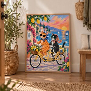 Puede incluir: Una lámina de arte enmarcada que muestra a un gato atigrado naranja y a un gato blanco y negro con gafas de sol y pañuelos, montando una bicicleta tándem amarilla. La escena incluye limones, flores rosas, un pueblo costero y el texto La Dolce Vita.