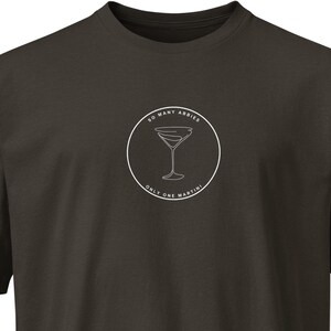 May include: Dark brown t-shirt with a white circular graphic featuring a martini glass and the text "SO MANY AMBIES, ONLY ONE MARTINI". The shirt has short sleeves and a crew neck.