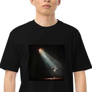 May include: Black t-shirt with a graphic of a martini glass under a spotlight. The image is centrally placed, with a dark backdrop and light beams. The t-shirt is worn by a person.