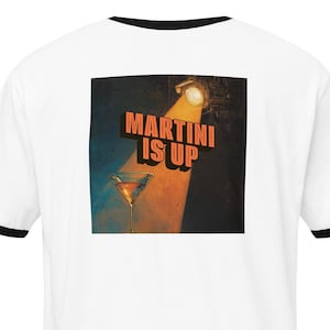 May include: White t-shirt with black trim on the collar and sleeves. The back of the shirt features a graphic of a martini glass under a spotlight, with the words "MARTINI IS UP" in orange letters.