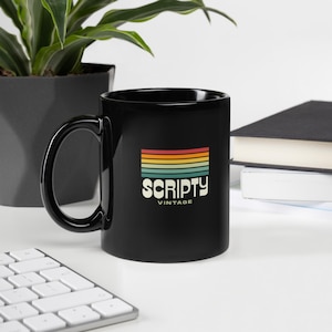Puede incluir: Taza de cerámica negra con asa curva. La taza presenta la palabra "SCRIPTY" en una fuente vintage, con un diseño de rayas arcoíris retro encima. La palabra "VINTAGE" está debajo.