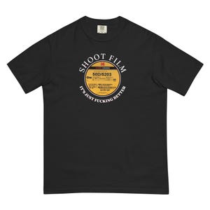 May include: Black t-shirt with a circular graphic featuring the text "SHOOT FILM" and "IT'S JUST FUCKING BETTER." The graphic resembles a film reel label, with the Kodak Visions logo and product information. The shirt is a comfortable, relaxed fit.