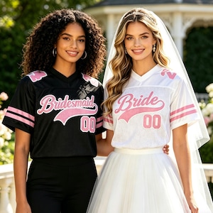 Peut inclure: Deux femmes portent des maillots de style football assortis. L'un est noir avec "Bridesmaid" en script rose et le numéro "00". L'autre est blanc avec "Bride" en script rose et le numéro "00". Les deux maillots ont des rayures roses.