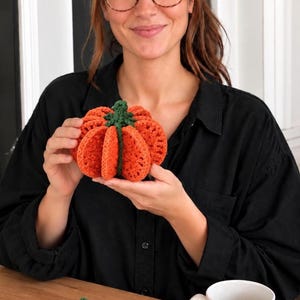 May include: A three-dimensional orange crochet pumpkin with a green stem, accompanied by two flat orange crochet pumpkin coasters and a white mug with the text Karen Crochet and a heart symbol. A circular label reads CROCHET PATTERN PDF.