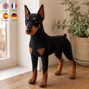 May include: A handcrafted crochet Doberman dog figurine featuring a black body with tan markings on the muzzle, chest, and legs. The toy has pointed ears, dark eyes, and a black nose, standing in a realistic pose with a textured yarn finish.