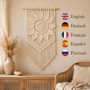 May include: A cream-colored macrame wall hanging featuring a large central flower design with radiating petals, suspended from a wooden dowel. To the right, a vertical list of five circular national flags with text labels for English, Deutsch, Français, Español, and Русский.